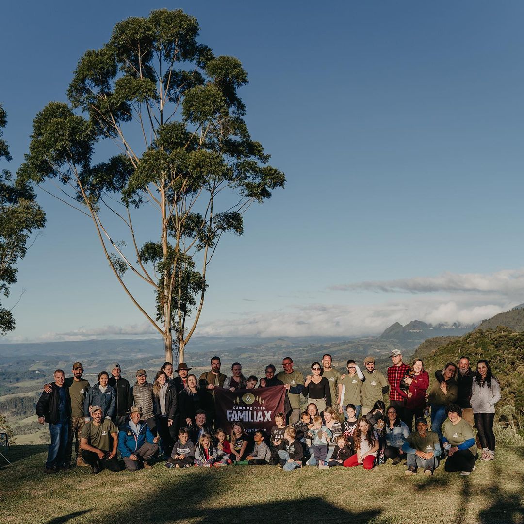 Um grupo grande de pessoas com uma bandeira do Camping da Família X